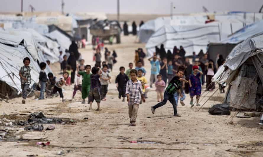 Children between a long row of tents in a refugee camp. Two children are throwing stones towards the photographer.