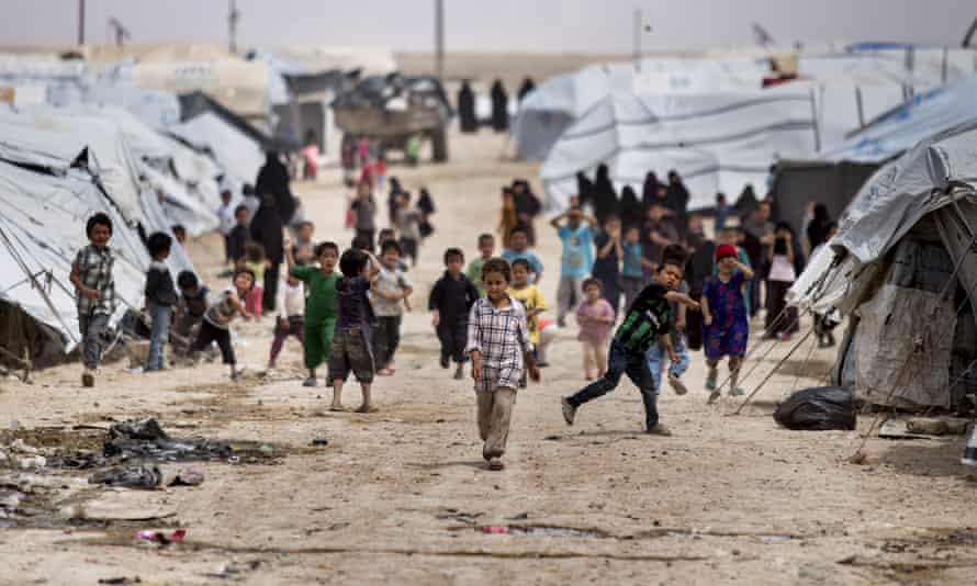 Children between a long row of tents in a refugee camp. Two children are throwing stones towards the photographer. 