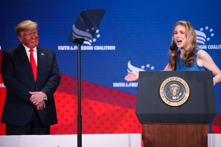 a woman speaks into a microphone while gesturing to a man nearby