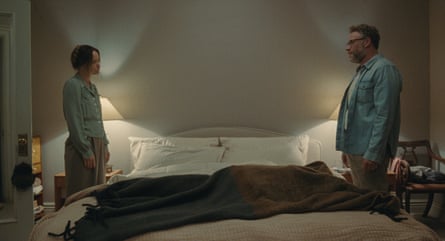 Wilde and Rogan face each other from opposite sides of a double bed, seeming far apart