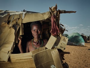 Mushina Mwaulatji olha para fora de um buraco no abrigo que ela construiu de papelão