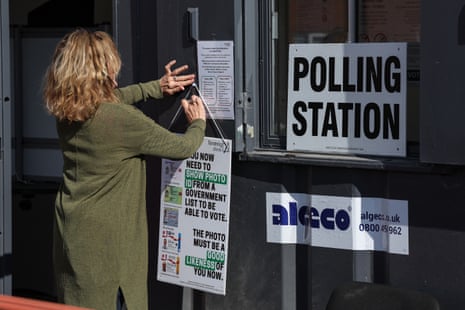 A polling clerk hanging up a sign reminding people to show ID as they turn up to vote in local elections at a mobile polling station in Walton-on-the-Naze, eastern England.
