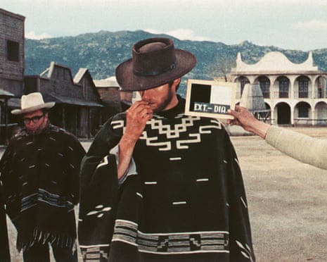 Clint Eastwood in a poncho next to an assistant holding a clapperboard with director Sergio Leone standing behind them also wearing a poncho