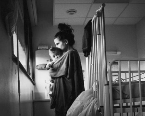 A woman holds her baby close to her face and looks out of a hospital window