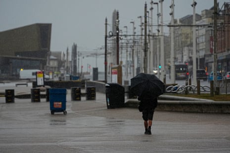 A man takes shelter from the wet weather beneath an umbrella as he walks along the promenade in Blackpool