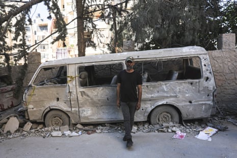 A man stands next to a damaged vehicle at the site of the strike.