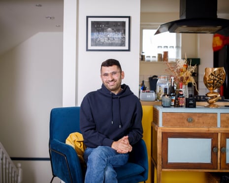 Michael Segalov at home, sitting in blue chair next to a sideboard with his luxuries