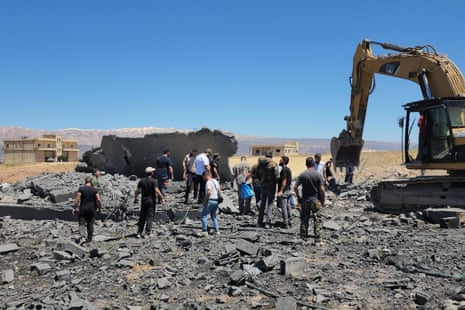Over a dozen men stand stood near heavy machinery at the site of a bombing.
