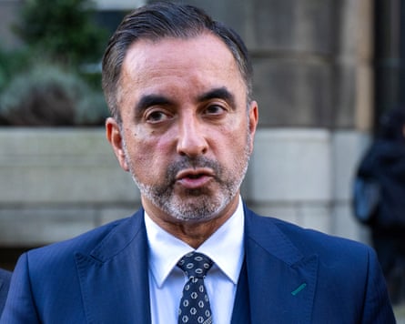 A man in a dark blue suit, solicitor Aamer Anwar, speaks to a group of journalists.