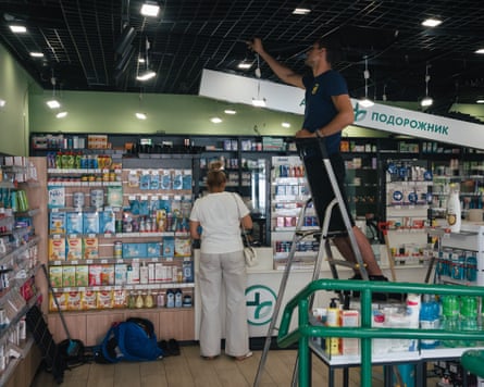 A man standing on a stepladder reaches up the ceiling as a woman stands next to the pharmacy counter
