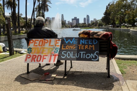 A homeless man sits on a bench adorned with protest signs at Echo Park Lake.