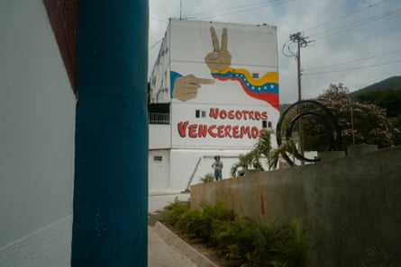 A woman standing in front of a mural of a hand giving the victory sign and a streamer in the colours of the Venezuelan flag
