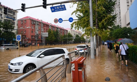 Passengers walk past cars submerged in flood water in the Mentougou district of Beijing on 31 July 2023