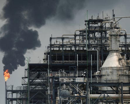 A large oil refinery with a flare and smoke billowing