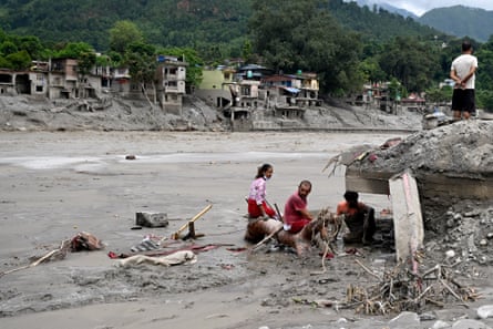 Two people sit on a tree branch in the mud, as two others look at the scene of devastation