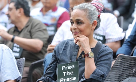 Arundhati Roy sits with a sign pinned to her shirt reading 'Free the Press'