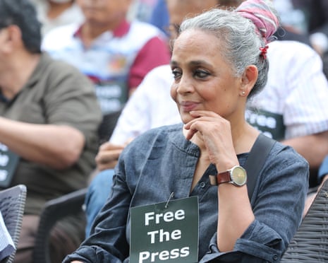 Arundhati Roy sits with a sign pinned to her shirt reading 'Free the Press'