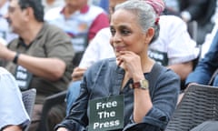 Arundhati Roy sits at a protest with a sign saying 'Free the press' attached to her shirt