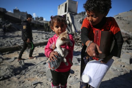 Palestinians children, one holding a cat, walk through the rubble of Aruba school in Nuseirat camp.