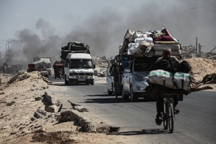 Cars and cyclists laden down with belongings on a road as smoke billows overhead