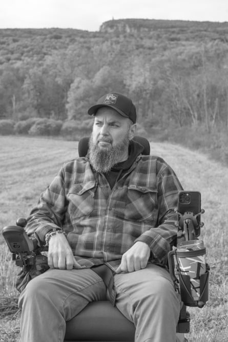A bearded man who is wearing a flannel and cap sits for a portrait in his Trackchair outside