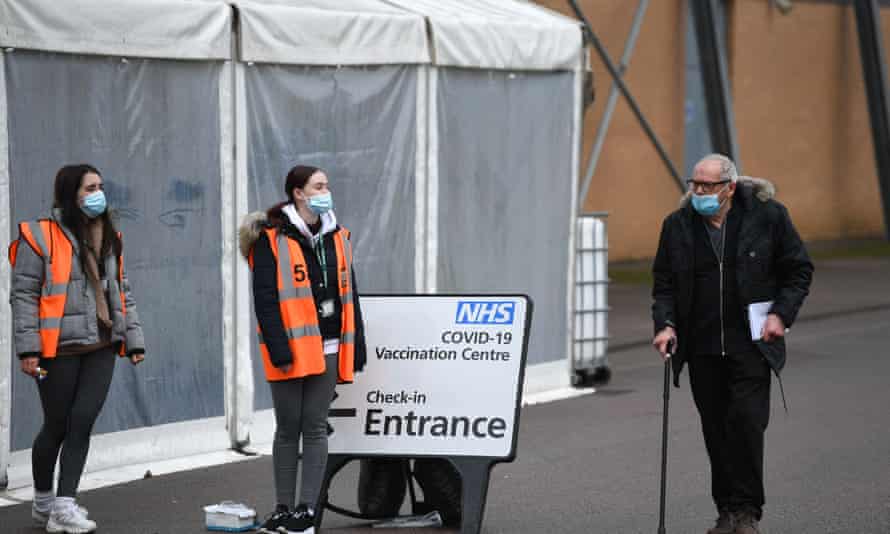 A man walks past volunteers at a temporary vaccination hub set up to administer a Covid-19 vaccine, at the Colchester Community Stadium in Essex on 6 February 2021.