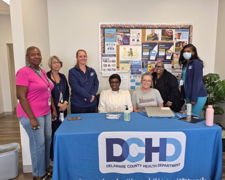 Seven people in a row , smiling, behind a desk with a cloth that says DCHD.