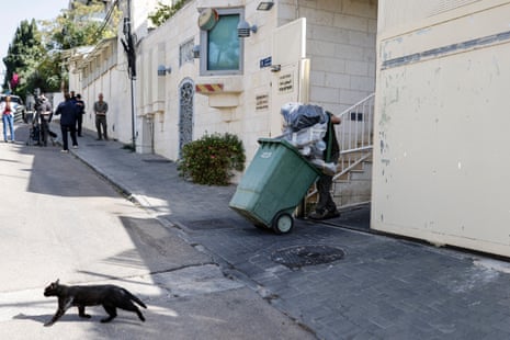 An employee wheels a rubbish bin as journalists stand nearby.