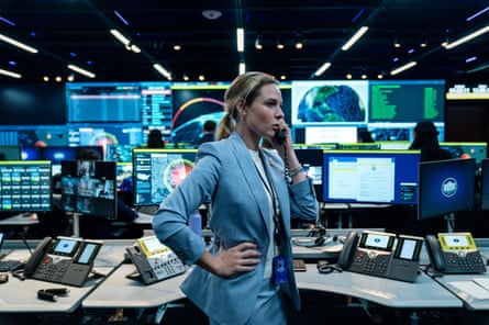 Rebecca Ferguson on the phone in a control room with many screens