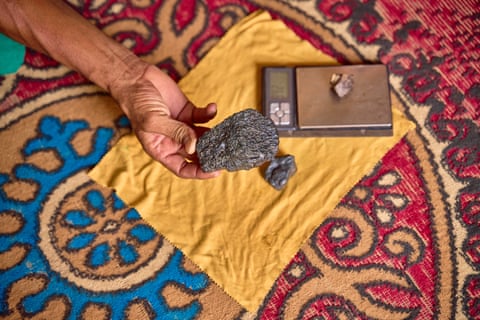 Hanoun’s hand holding a grey piece of rock over a yellow cloth laid on a colourful rug