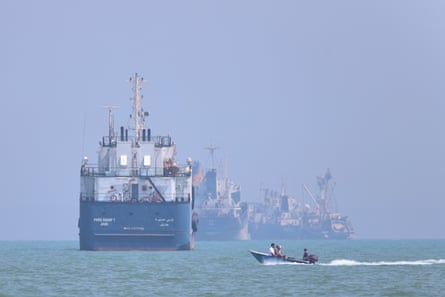 A motorboat passes large ships anchored in the Strait of Hormuz