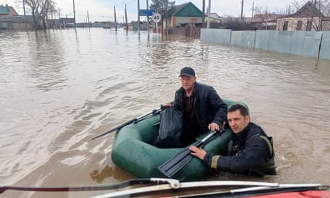 A rescuer guides a dinghy carrying an older man through high flood waters