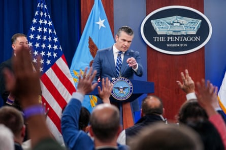 man in suit standing at lectern points finger toward people raising hands