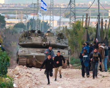 Palestinian children and journalists disperse as Israeli tanks approach along a dirt road
