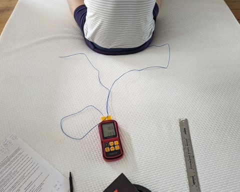 O persoană stă în partea de sus a cadrului, așezată în pantaloni scurți, în centrul saltelei, iar pe saltea sunt afișate un gadget, un pix, o foaie cu informații și o riglă metalică.