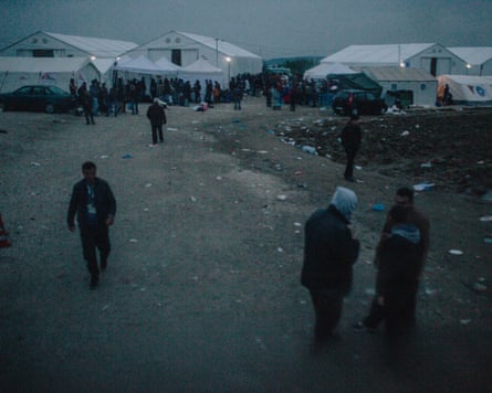 People stand outside tent structure at an open‑air camp for refugees at the Greek border with North Macedonia.