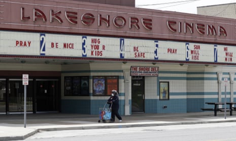 A woman wearing a mask walks with her groceries past a closed Lakeshore Cinema theatre in Euclid, Ohio.