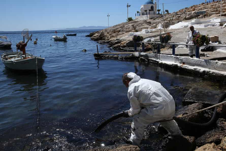 Workers struggle to remove an oil spill from a beach in the coastal zone of Athens, Greece
