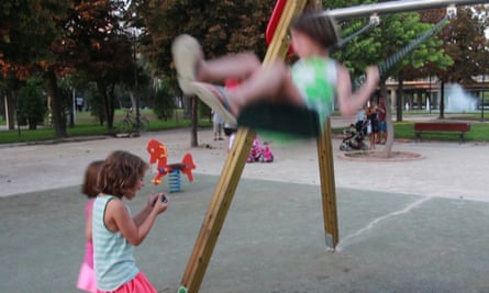 One child plays on swing while another plays with Hybrid Play app on a smartphone.