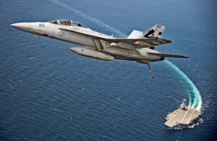 An F/A-18F Super Hornet jet flies over the USS Gerald R. Ford