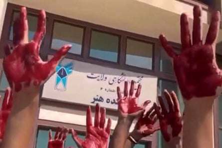 Iranian students raise hands painted red outside a university building.