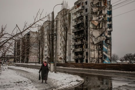 An elderly woman walks by the snow-covered rubble of a residential building in Borodianka