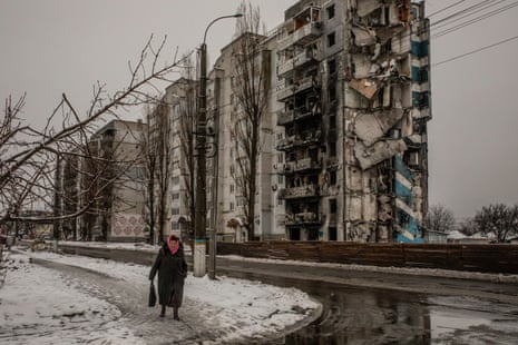 An elderly woman walks by the snow-covered rubble of a residential building in Borodianka
