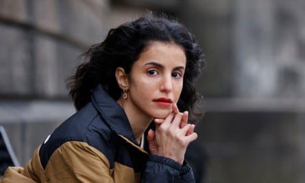 A young Arab woman in western dress sits on a bench outside a stone building