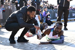 The runner, lying on the ground, is handed a water bottle