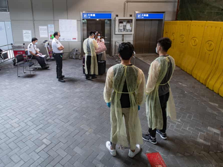 Workers wearing personal protective equipment (PPE) assist arriving passengers to board a bus to a coronavirus testing facility in Hong Kong.