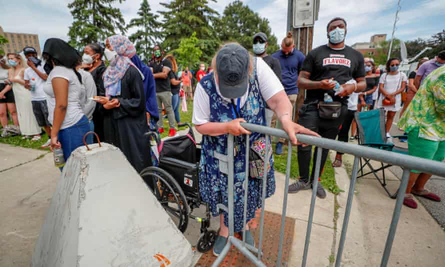 A woman in a wheelchair leans on a street barricade as people outside the memorial for George Floyd are asked to stand for nine minutes in memory of his death.