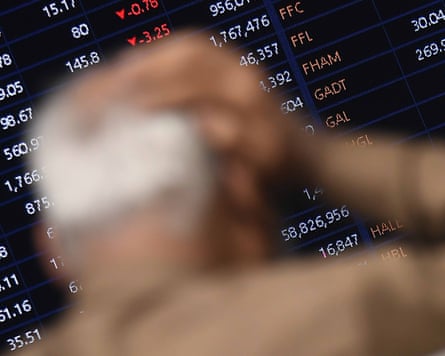 A man scratches his head while looking up at a board listing stock prices
