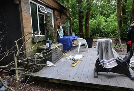 A cabin in woodland with a wooden deck and plastic furniture