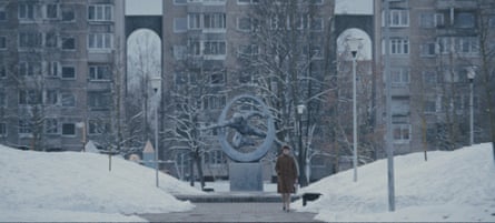 A woman walks through a snowy concourse in front of a Soviet statue.
